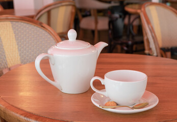 White porcelain teapot and tea cup stand on a table in a cafe. Horizontal orientation, selective focus.