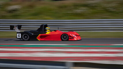 Fototapeta na wymiar A panning shot of a red and black racing car as it circuits a track.