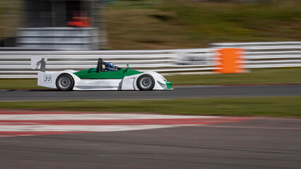 A panning shot of a white and green racing car as it circuits a track.