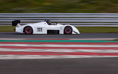 A panning shot of a white racing car as it circuits a track.