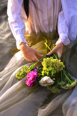 A bouquet of wild flowers in female hands on the water