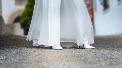 The bride with long dress shows her white wedding shoes