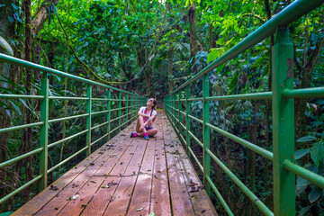 Fototapeta na wymiar Young woman sitting on the bridge in the jungle. Mistico Arenal Hanging Bridges Park in Costa Rica, Central America. Cloud forest.