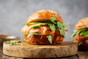 Burger sandwich with salmon, cream cheese, avocado and arugula on a light background, concept diet food, sandwich take away, healthy fast food