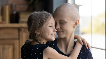 Happy young Caucasian cancer patient sick mother and little daughter hug show love and care,...