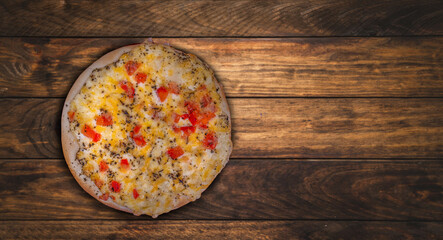 pizza with cheese and vegetables lies on a dark wooden table. space for text