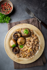Buckwheat porridge with mushrooms in a plate on black background, top view