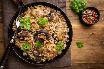 Buckwheat porridge with mushrooms in the frying pan on wooden table, top view