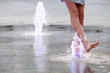 a girl touches a fountain on the sidewalk with her bare foot