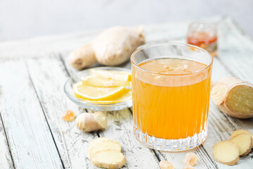 Yellow drink with ginger, lemon and ice in a glass, refreshing homemade ginger lemonade or ale on white background