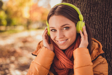 Closeup headshot photo of pretty charming lady beaming smiling sitting ground among yellowed leaves autumn park listen chilling music wear headphones scarf orange windbreaker outside