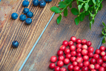 Forest berries on dark rustic wooden background. Cranberries and blueberries with green leaves on old wooden table. Top view.