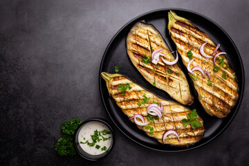 Grilled eggplant slices, garnished with fresh herbs, on black background, top view