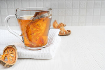 Traditional beneficial matoom tea made of dried bael fruit slices, also known as wood apple, in transparent glass cup on towel on white wooden background. Image with copy space and selective focus