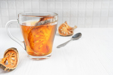 Asian healing matoom tea made of dried bael fruit slices, also known as wood apple, in transparent glass cup on white wooden background at kitchen. Image with copy space and selective focus
