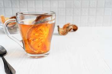 Traditional thai matoom tea made of dried bael fruit slices, also known as stone apple, in glass cup at kitchen on white wooden background with spoon. Image with copy space and selective focus