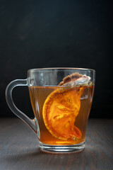 Single glass cup of Thai traditional healing matoom tea made of dried bael fruit slices, also known as stone apple, on dark brown wooden background. Vertical orientation