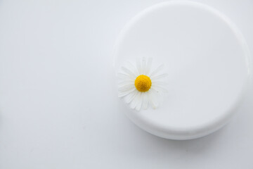 Fototapeta na wymiar White jar of moisturizer and chamomile flowers on a white background.