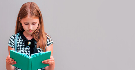 Young school girl reading a book on gray background