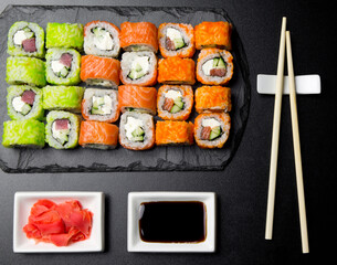 Sushi set served on a stone slate on a dark background. Sushi rolls with salmon, tuna, cucumber, wasabi, soy sauce and ginger. Sushi rolls photo for menu and advertising