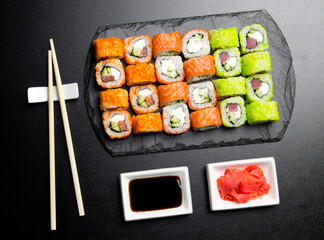 Sushi set served on a stone slate on a dark background. Sushi rolls with salmon, tuna, cucumber, wasabi, soy sauce and ginger. Sushi rolls photo for menu and advertising