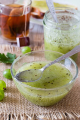 Gooseberry jam in bowl, glass and cup of tea