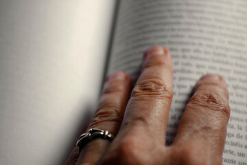 Primer plano de unos dedos de mujer mayor sobre un libro abierto.