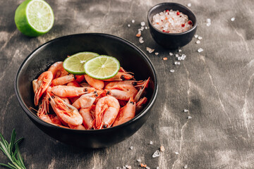 Top view of bowl with boiled shrimps with lime in black bowl on dark background.