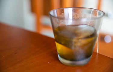 Close-up image of a cold herbal tea: the glass is covered with condensation. The sachet is infused in the glass.