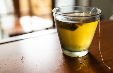 Close-up image of a cold herbal tea: the glass is covered with condensation. The sachet is infused in the glass.
