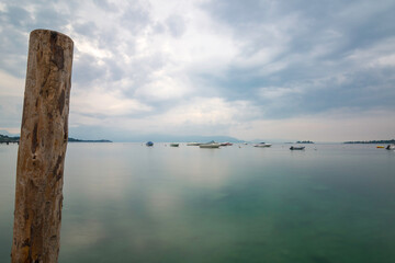 View of Lake Garda in the early morning or evening. The water is calm, the sky is partly cloudy. Small boats dance on the water. The mood is dreamy. morning Mood