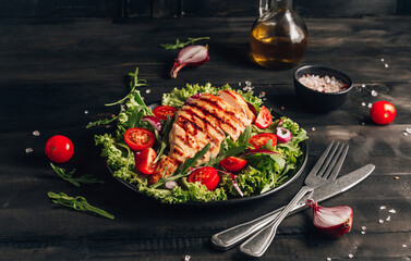 Grilled chicken fillet and fresh vegetable salad of tomatoes and arugula leaves. Healthy food. Black background.