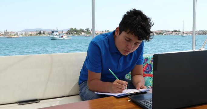Teenage boy studying on yacht deck Online learning education distance learning for kids at home Homeschooling during quarantine or isolation