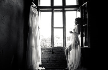 Black and white portrait of an elegant bride standing in front of a window holding a glass of champagne.