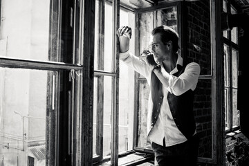 Black and white portrait man in a green suit sitting on a table near the window holding a glass of...