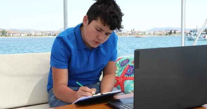 Teenage boy studying on yacht deck Online learning education distance learning for kids at home Homeschooling during quarantine or isolation