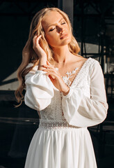 Fototapeta premium Portrait of an elegant blonde in a white dress on a background of a modern building.
