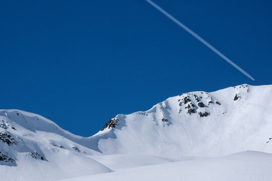 Airplane contrail in sunny blue sky above snowy mountain, Davos, Canton of Graubuenden, Switzerland