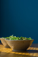 Tuna salad in a ceramic bowl on a wooden table on a dark blue background.