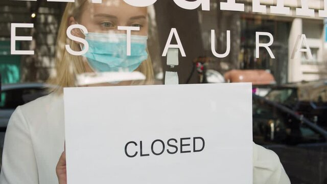 cafe or restaurants and business closed banking financial crisis after coronavirus quarantine is over. woman with face mask turning sign for rent to door shop. small business sale after post covid