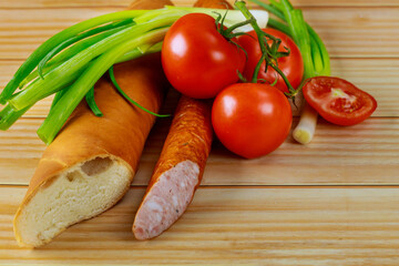 Bread, tomatoes and kielbasa with chives on wooden background.