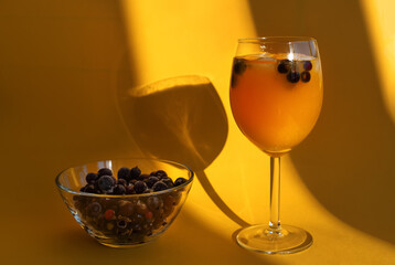 A glass of homemade quarantini cocktail and a bowl of berries against a yellow wall, in the rays of the setting sun. The concept of the new popular drinks. Close-up, shadows, space for text. 