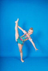 Fototapeta premium a beautiful gymnast girl in a suit stands in a pose for balance on a blue isolated background with space for text