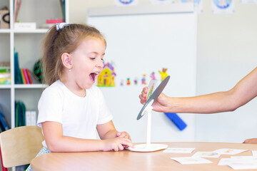 developmental and speech therapy classes with a child-girl. Speech therapy exercises and games with a mirror and cards