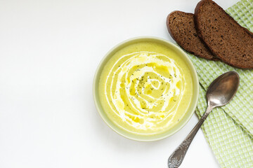 Cream-broccoli soup with cream and olive oil, in a green Cup, on a white background, with a green napkin and homemade bread. Top view, horizontal position, space for text