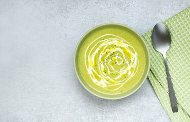 Fragrant, homemade broccoli cream soup with cream, olive oil and spices in a green plate on a gray table. Green napkin and spoon. Top view, horizontal, copy space