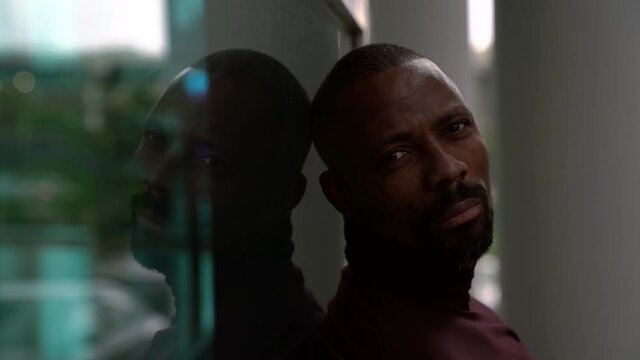 Close-up portrait of a sad bearded middle-aged African-American man posing on the street leaning against a reflecting large window