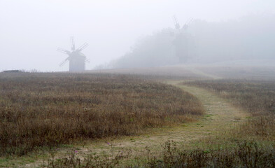 Fototapeta na wymiar Country road on a hill in the middle of a field with windmills in the fog.