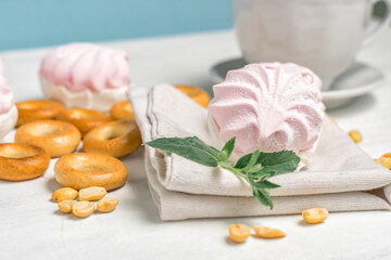 sweets and a cup of tea. marshmallow, bagels and nuts with a mint leaf. composition on a light background with blur. selective focus.