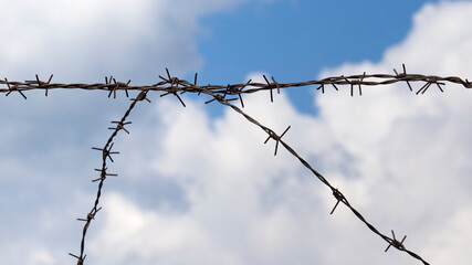 Fototapeta na wymiar Close-up view of old rusty barbed wire on an old concrete wall, blue sky with white clouds in the background. Symbol of lost freedom